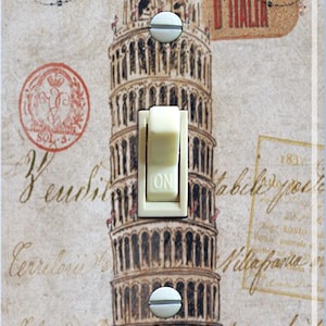 Puede incluir: Una tapa de interruptor de luz con una ilustración vintage de la Torre Inclinada de Pisa en Italia. La tapa tiene un interruptor de palanca blanco con la palabra "ON" impresa en él. El fondo es de color crema con texto marrón y negro.