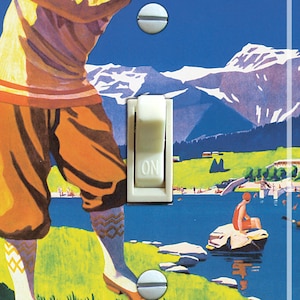 May include: A vintage-style light switch cover featuring a golfer swinging a club in a mountain landscape. The switch is labeled "ON" and the scene includes a lake, trees, and the word "TRUCKEE".
