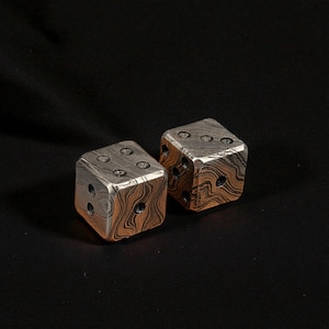 Puede incluir: Dos dados de metal con un dise&ntilde;o &uacute;nico. Los dados tienen una combinaci&oacute;n de colores plateado y marr&oacute;n, con los n&uacute;meros representados por agujeros perforados. Los dados est&aacute;n colocados sobre un fondo oscuro.