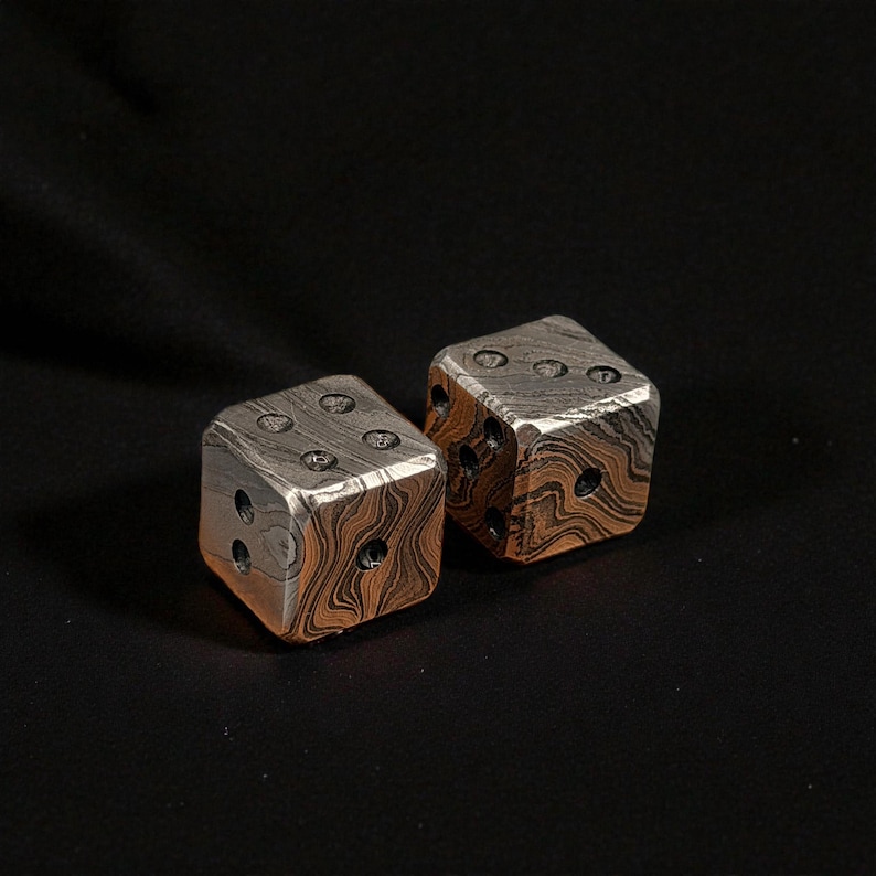 Puede incluir: Dos dados de metal con un dise&ntilde;o &uacute;nico. Los dados tienen una combinaci&oacute;n de colores plateado y marr&oacute;n, con los n&uacute;meros representados por agujeros perforados. Los dados est&aacute;n colocados sobre un fondo oscuro.