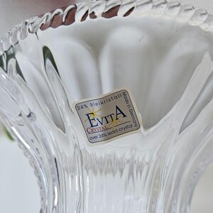 May include: Close-up of a clear crystal vase with a fluted design. The vase has a label that reads "Evita Crystal" and "24% Bleikristall, over 24% lead crystal, Made in Germany."