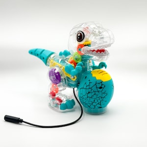 以下が含まれることがあります： 内部の歯車が見える、透明なプラスチック製の恐竜のおもちゃ。 ターコイズと黄色の配色です。 恐竜はターコイズの尾、手足、アクセントがあり、ひびの入った卵型のベースが付いています。 黒いコードがベースから伸びています。