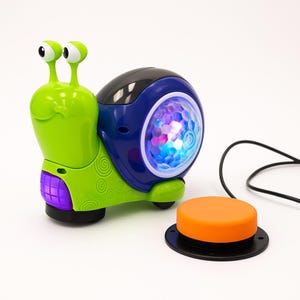 以下が含まれることがあります： 緑色の体、青い殻、光るディスコボールが付いたカラフルなおもちゃのカタツムリ。カタツムリには、黒いワイヤーで接続されたオレンジ色のボタンが付いています。子供向けのおもちゃです。