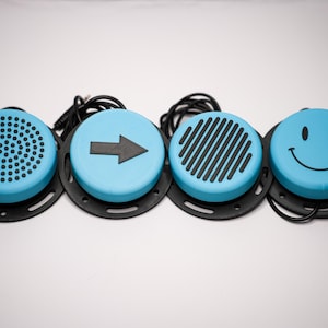 May include: Four light blue circular devices with black bases and attached cords. Each device has a different design: a grid of holes, an arrow, diagonal lines, and a smiley face. The devices are on a white surface.