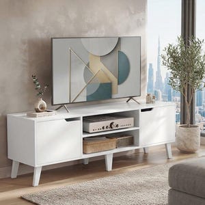 May include: A white television stand with four tapered legs, two side cabinets with cutout handles, and two open center shelves. The stand holds a flat-screen television displaying a geometric pattern, a small vase, and electronic equipment.