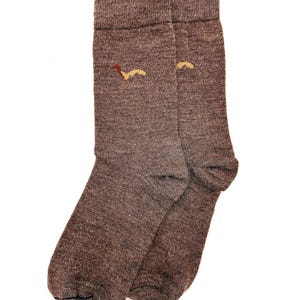 May include: A pair of brown socks with a small, abstract design in shades of brown and yellow near the top. The socks are made of a textured material and are displayed against a white background. The socks are a neutral color.