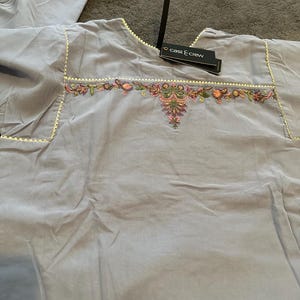 以下が含まれることがあります： ピンク、緑、オレンジの花柄刺繍が施された薄紫色のチュニック。 チュニックはスカラップトリムで、「cast & crew」と書かれたタグが付いています。 生地は柔らかく、軽量に見えます。