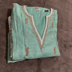 May include: A turquoise blue tunic with gold and silver embroidery. The tunic has a V-neck and is made of a lightweight fabric. The label on the tunic reads "Khaadi".