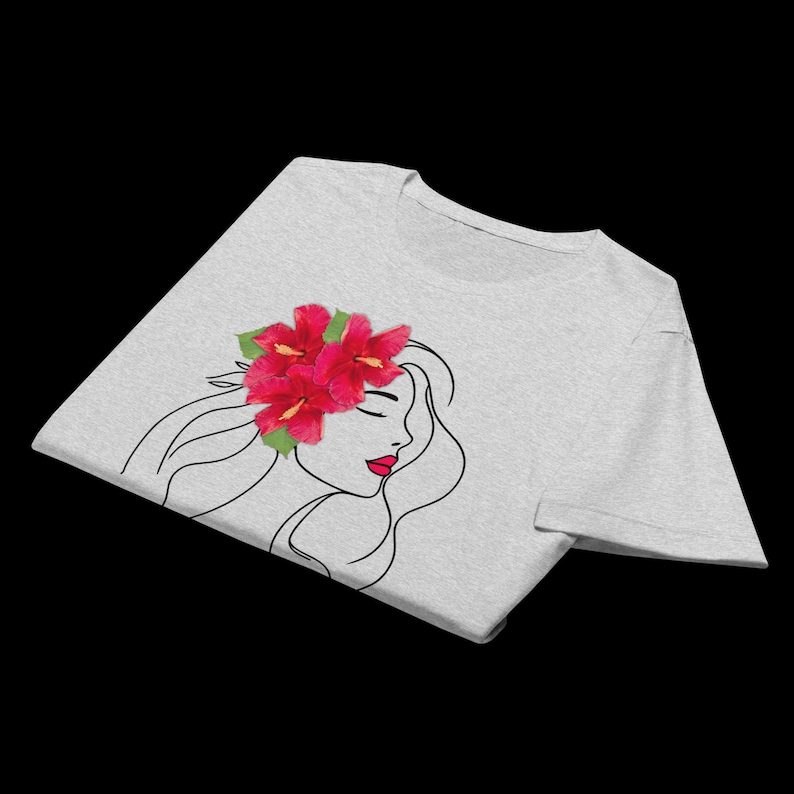 Puede incluir: Camiseta gris claro con un dibujo lineal minimalista del perfil de una mujer. La mujer tiene una flor de hibisco roja en el pelo y pintalabios rojo. La camiseta est&aacute; hecha de un material suave.