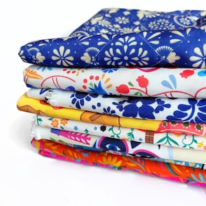 Pode incluir: Uma pilha de tecido colorido com estampas florais e geométricas. Os tecidos são em tons de azul, branco, amarelo, laranja e rosa. Os padrões incluem flores, folhas e formas geométricas. Os tecidos são dobrados e empilhados.