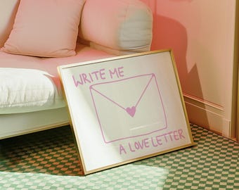 May include: A framed print with the words "WRITE ME A LOVE LETTER" in a handwritten style. The image features a pink envelope with a heart, set against a white background. The frame is gold.