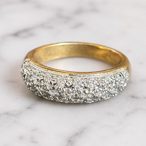 May include: A gold band ring featuring a wide, rounded front section encrusted with numerous small, clear, faceted stones set in a silver-toned metal. The back portion of the ring is a smooth, polished yellow gold band, creating a two-tone appearance.
