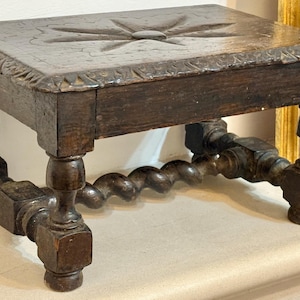 Può includere: Sgabello antico in legno marrone scuro, con un motivo a stella intagliato sulla parte superiore. Le gambe sono intagliate con dettagli torniti e a spirale. Di forma rettangolare.