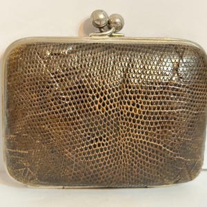 May include: A rectangular, vintage brown clutch with a textured, reptile-like pattern. The clasp and frame are silver-toned. The clutch has a rounded shape and a small, double-ball clasp.