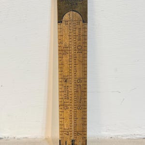 Puede incluir: Una regla plegable de madera vintage con herrajes de latón. La regla está marcada con el texto "R.W. OGDEN 1922" y medidas en centímetros. La regla está plegada y muestra medidas de 15 a 43 cm.