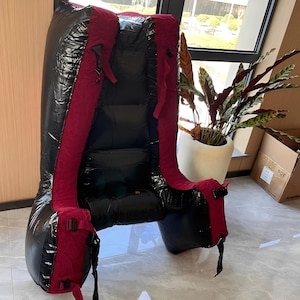 May include: A large, black inflatable chair with burgundy straps and accents. The chair has a high back and armrests, and is designed for comfort and support. The chair is made of a shiny, durable material and is suitable for indoor or outdoor use.