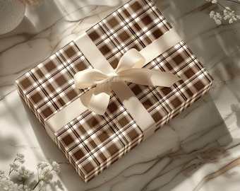 Puede incluir: Un regalo envuelto en papel a cuadros marrón y blanco, atado con una cinta y un lazo de satén color crema. El regalo se presenta sobre una superficie de mármol, con iluminación suave y detalles florales.