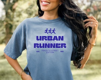 May include: A blue t-shirt with the words "URBAN RUNNER" in purple block letters. Above the text is a graphic of three running figures. The shirt also includes the text "MILES OF LIFE" and "TRACK TO STREET EDITION".