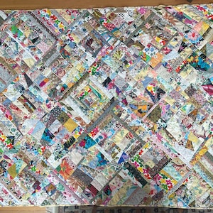 May include: A patchwork quilt with a vibrant mix of floral and geometric patterns. The quilt features a variety of fabrics in shades of pink, blue, yellow, and green, arranged in a diagonal design. The quilt is a cozy home decor item.