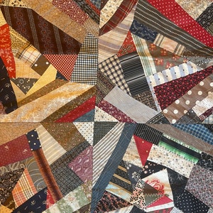 May include: A patchwork quilt with a variety of fabric patterns and colors. The quilt features geometric shapes and a mix of stripes, polka dots, and floral designs in shades of brown, red, blue, and cream.