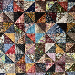 May include: A patchwork quilt with a geometric design. The quilt is composed of numerous fabric triangles in various colors and patterns, including paisley, floral, and solid textures. The color palette includes blues, reds, browns, and greens.