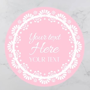 May include: A round, pink sticker with white floral lace trim. The sticker has the words "Your text Here" and "YOUR TEXT" in white script. The background is a marble pattern.