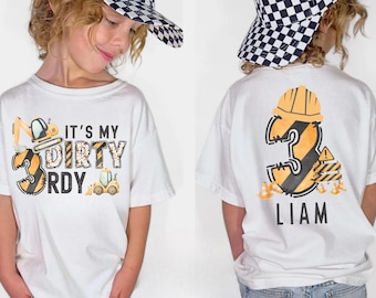 May include: White t-shirt with a construction-themed design. The front features the text "It's My Dirty 3rd B-Day" with construction vehicle graphics. The back displays a large number 3 with a construction hat and the name "Liam".