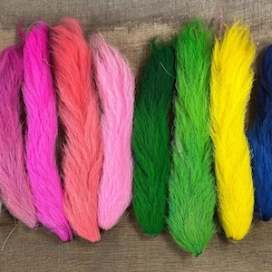 Könnte beinhalten: Eine Sammlung farbig gefärbter Federn in Weiß, Rosa, Rot, Grün, Gelb und Blau. Die Federn sind auf einer Holzoberfläche angeordnet und zeigen ihre leuchtenden Farben und ihre weiche Textur. Ideal für Bastelprojekte.