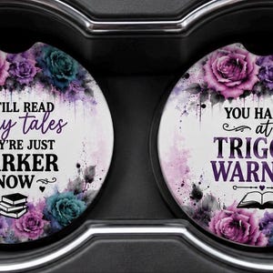 May include: Two circular car cup holder coasters featuring purple and teal roses. The left coaster reads I STILL READ fairy tales THEY'RE JUST DARKER NOW with a stack of books. The right coaster reads YOU HAD ME AT TRIGGER WARNING with an open book.
