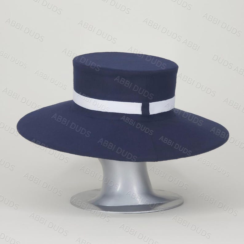 Pu&ograve; includere: Un cappello blu navy con parte superiore piatta e tesa larga. Il cappello presenta un nastro bianco che circonda la base della corona. Il design &egrave; semplice e strutturato, mostrando un colore blu scuro solido contrastato dal dettaglio bianco.