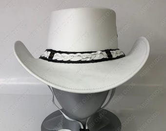 May include: A white cowboy hat with a braided black and white band. The hat has a wide brim and a tall crown. A chin strap is attached to the hat. The hat is displayed on a gray mannequin head.