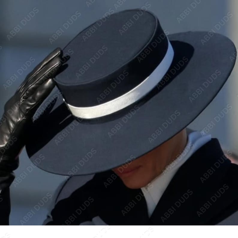 Pu&ograve; includere: Un cappello nero a corona piatta con una tesa larga e circolare e un nastro bianco a contrasto che circonda la base della corona. Il cappello &egrave; realizzato con una finitura opaca liscia e mantiene una silhouette rigida e strutturata.