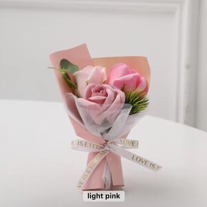 K&ouml;nnte beinhalten: Ein kleiner Strau&szlig; hellrosa Rosen, eingewickelt in rosa Papier und wei&szlig;em Netz. Der Strau&szlig; ist mit einem Band gebunden, auf dem "LOVE IS ETERNAL" steht. Der Text "light pink" steht unten.