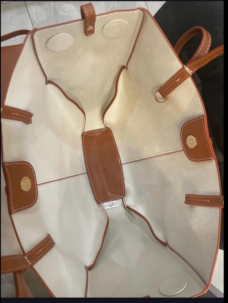 Puede incluir: Un bolso tote marr&oacute;n con interior beige claro. El bolso presenta asas, ribetes y un cierre magn&eacute;tico marrones. El interior tiene un dise&ntilde;o estructurado con un bolsillo central y compartimentos laterales.