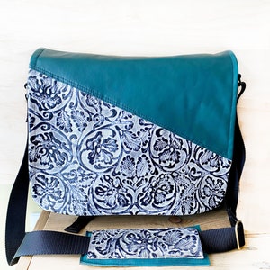 May include: A teal messenger bag with a floral pattern on the front flap and a matching strap pad. The bag has a diagonal color block design with teal on the top and a floral pattern on the bottom. A matching wallet is also included.