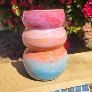 May include: A stack of three ceramic bowls in shades of pink, orange, and blue. The bowls are stacked on top of each other, creating a unique and artistic display. The colors blend together, creating a gradient effect. The bowls are likely handmade and suitable for home decor.