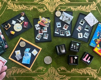 May include: A collection of miniature items including small black trays with tiny photographs, a miniature VHS tape labeled Frankenstein, a miniature box labeled Trojan, small black boxes containing tiny adult toys, and a miniature magazine.