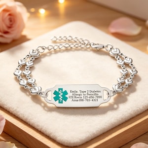 May include: A silver medical alert bracelet featuring a double chain of small heart-shaped links. The central rectangular tag displays a teal Star of Life symbol and engraved text: Emily, Type 2 Diabetes, Allergic to Penicillin, ICE:Kevin 123-456-7890, Anna:098-765-4321.