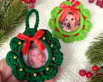 May include: Two handmade Christmas ornaments. One is green with a red bow and a photo of a child. The other is lime green with a red bow and a photo of a dog. Both are crocheted in a wreath design with red and gold accents.