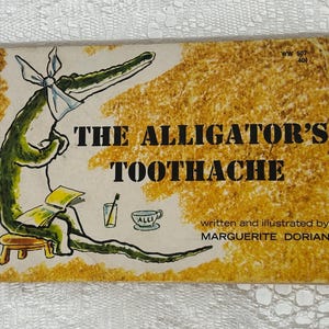 May include: Vintage children's book titled "The Alligator's Toothache." The cover features a cartoon alligator with a toothache, wearing a bandage. The background is a textured yellow-brown color. The author's name is also on the cover.