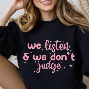 Könnte beinhalten: Schwarzer Pullover mit dem Text "We listen & we don't judge" in rosa Schrift mit einem Glitzer-Design.