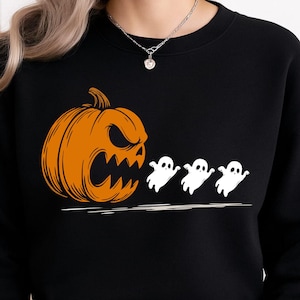 May include: Black sweatshirt featuring a Halloween design. An orange pumpkin with an angry face is on the left, with three white ghost figures to the right. The design is a line drawing style.