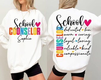 May include: A white long-sleeve sweatshirt featuring a colorful graphic. The front displays the text School COUNSELOR Sophia with a pink heart. The back features the text School COUNSELOR with words like dedicated, fun, warm, caring, loyal, loving, reliable, kind, and compassionate.