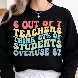 May include: Black sweatshirt with the text "6 OUT OF 7 TEACHERS THINK 67% OF STUDENTS OVERUSE 67" in retro-style, colorful lettering. The text is in red, yellow, turquoise, and green. A casual, comfortable garment.