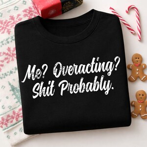 May include: A black crewneck sweatshirt featuring white distressed-style text printed on the front that reads, "Me? Overacting? Shit Probably." The garment has a classic long-sleeve design with a ribbed collar, cuffs, and hemline.