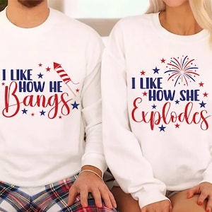Puede incluir: Dos sudaderas blancas de cuello redondo con texto gráfico en rojo y azul y detalles de estrellas. La sudadera izquierda muestra el texto I LIKE HOW HE Bangs con un cohete. La sudadera derecha muestra I LIKE HOW SHE Explodes con un fuego artificial.