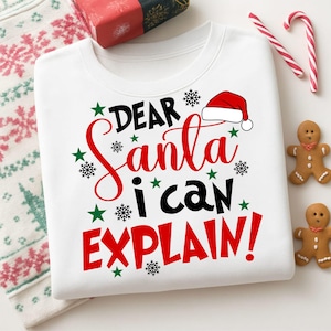 May include: White sweatshirt with the text "DEAR Santa i can EXPLAIN!" in red and black, with a Santa hat graphic. Green stars and snowflakes decorate the design. Candy canes and gingerbread men are also visible.