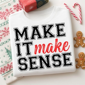 May include: White sweatshirt with the text "MAKE IT make SENSE" in black and red. The sweatshirt is surrounded by holiday-themed items, including candy canes, gingerbread men, and a wrapped gift.