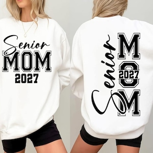 May include: A white long-sleeve sweatshirt featuring black text. The front displays 'Senior MOM 2027' in a mix of script and block lettering. The back features the word 'Senior' in script, with 'MOM' in block letters and '2027' centered inside.