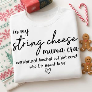 Könnte beinhalten: Weißes Sweatshirt mit schwarzem Schriftzug: "in my string cheese mama cra overwhelmed touched out but exact who I'm meant to be". Das Bild enthält ein Geschenk, Zuckerstangen und Lebkuchenmänner.
